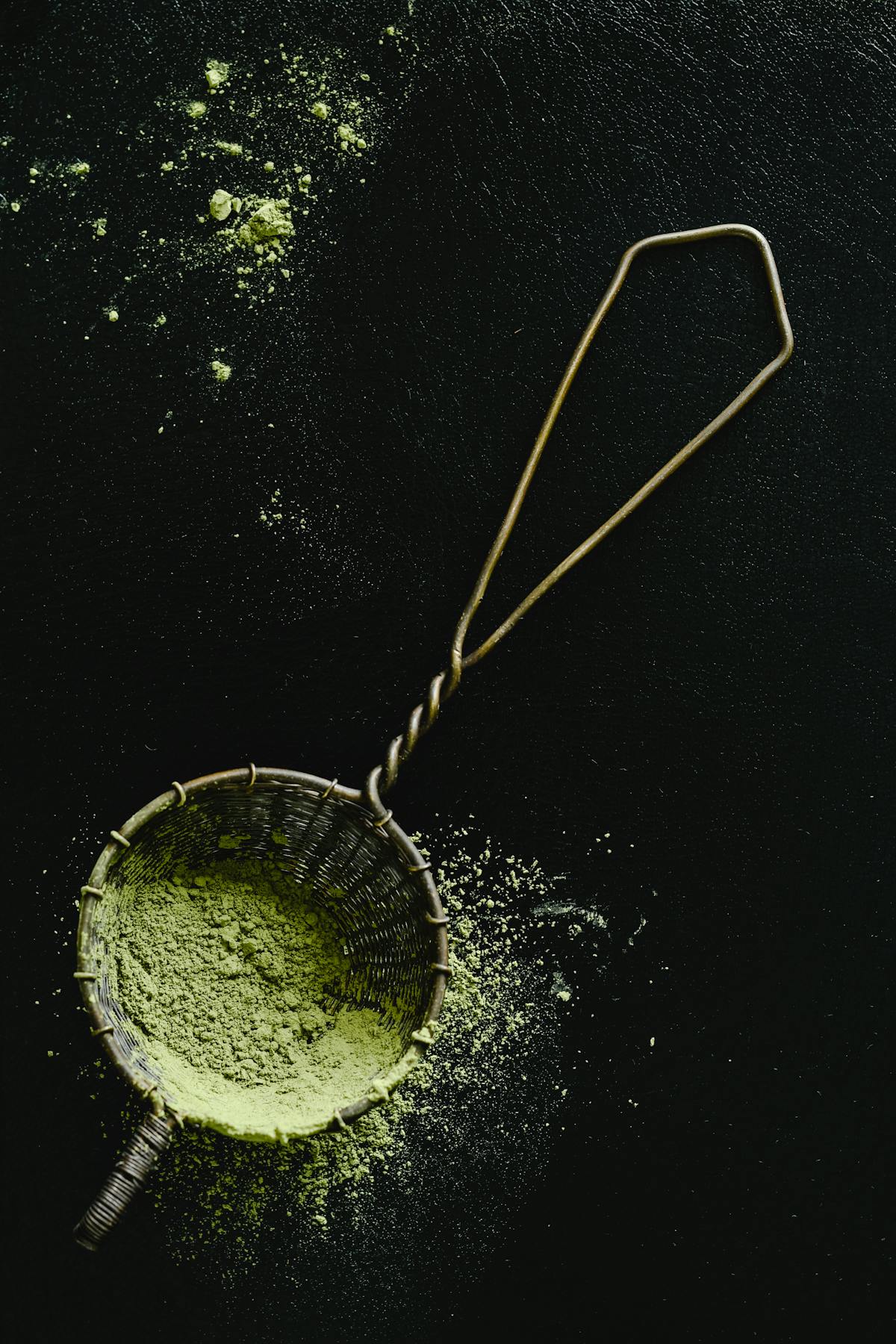 Green supplement powder scattered from a sieve on a dark surface